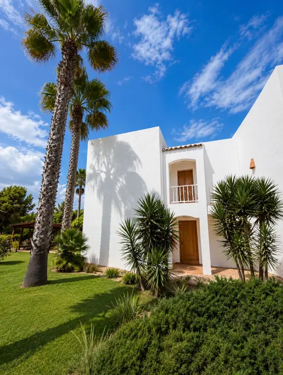 Fachada encalada de una de las casas, con palmeras y jardín